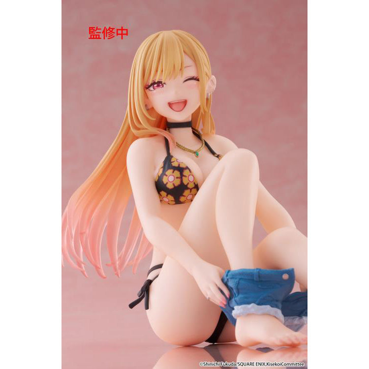 Figure of Marin Kitagawa from My Dress-Up Darling sitting and smiling in a black floral swimsuit, holding blue shorts while posing playfully on a pink background.