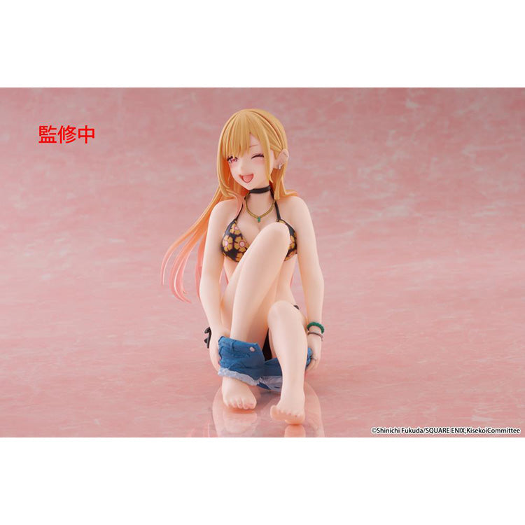 Figure of Marin Kitagawa from My Dress-Up Darling sitting and smiling in a black floral swimsuit, holding blue shorts while posing playfully on a pink background.