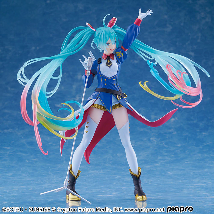 A high-quality frontal shot of the Gundam x Hatsune Miku figure against a solid blue background, emphasizing the translucent clear parts and 4-color gradient of her hair.