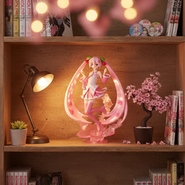 Sakura Miku BANPRESTO EVOLVE Vocaloid figure with cherry blossom pink hair and outfit by Bandai Spirits displayed on a bookshelf with manga and anime pin badge