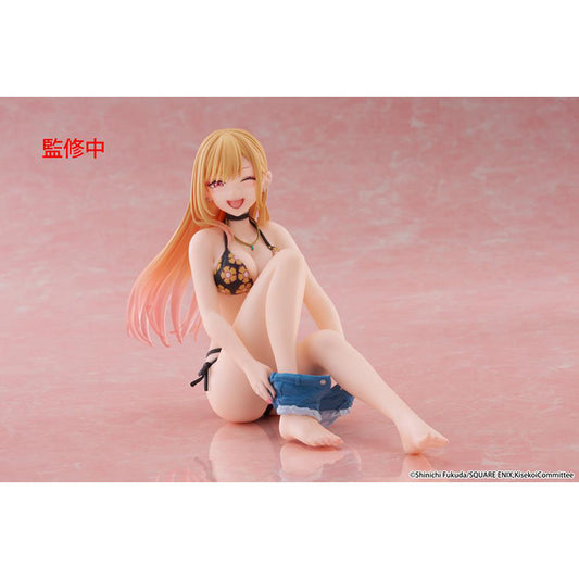 Figure of Marin Kitagawa from My Dress-Up Darling sitting and smiling in a black floral swimsuit, holding blue shorts while posing playfully on a pink background.