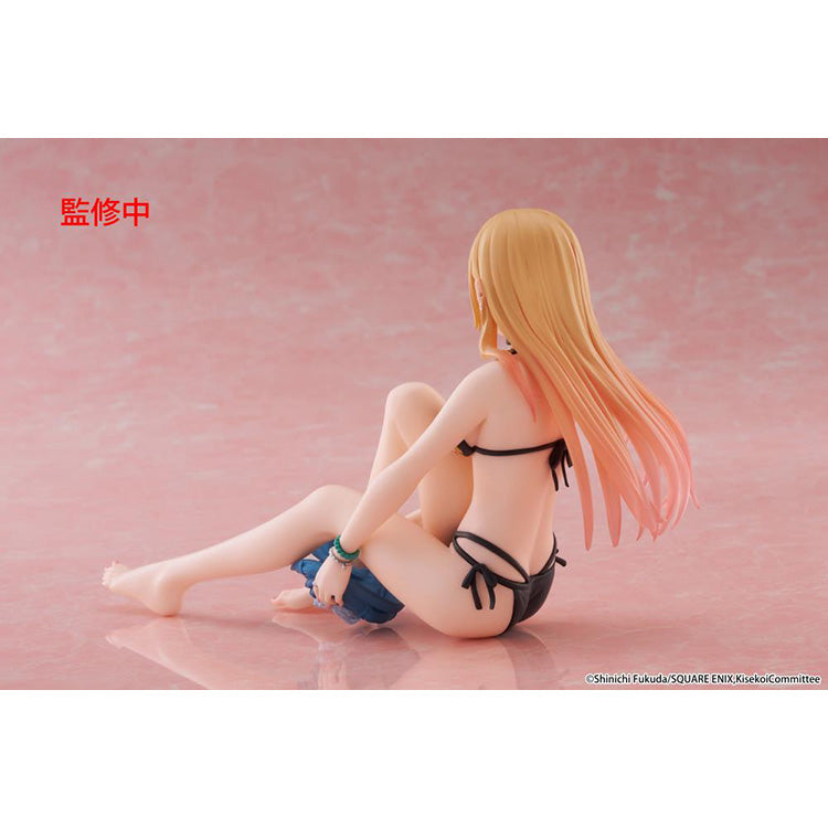 Figure of Marin Kitagawa from My Dress-Up Darling sitting and smiling in a black floral swimsuit, holding blue shorts while posing playfully on a pink background.
