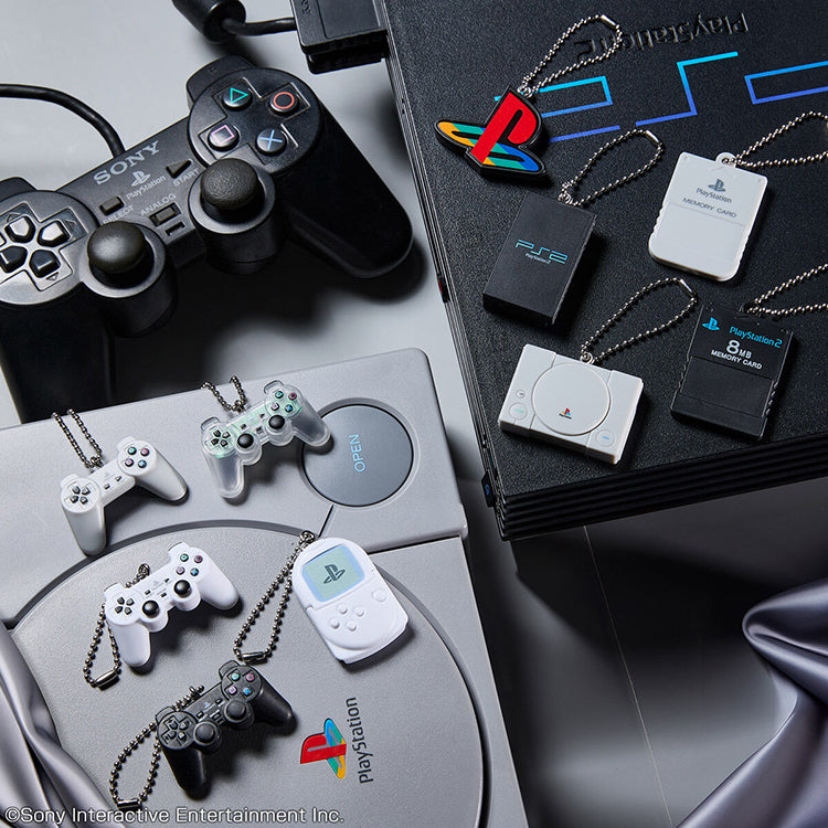 Retro PlayStation miniature keychain charms of PS1 and PS2 hardware, controllers, and memory cards on consoles.